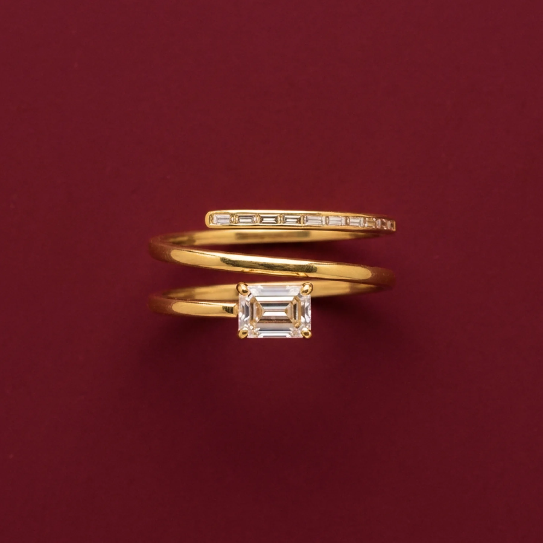 A stack of warm-gold rings with baguette diamonds on burgundy velvet.