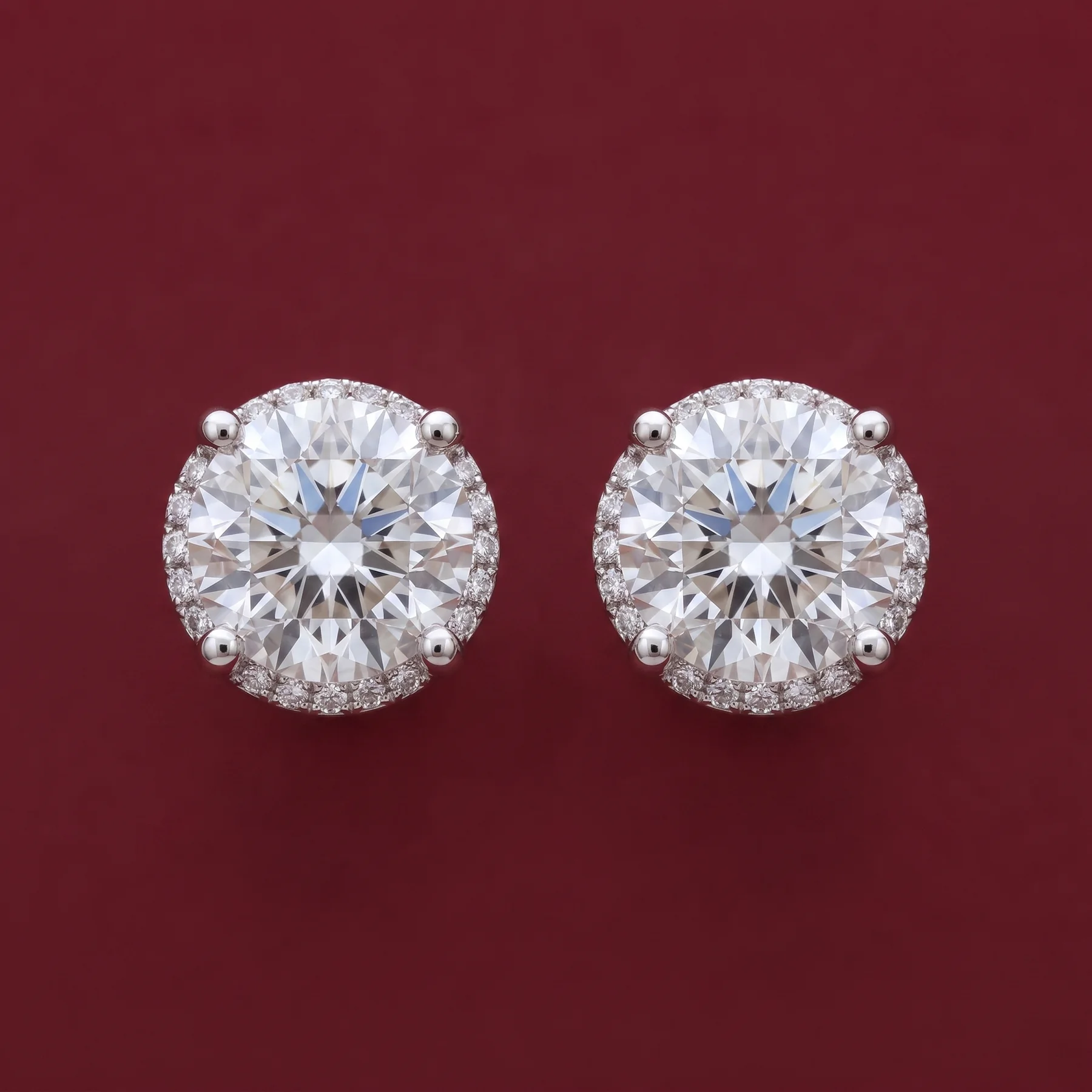 A pair of diamond companion stud earrings on burgundy velvet.